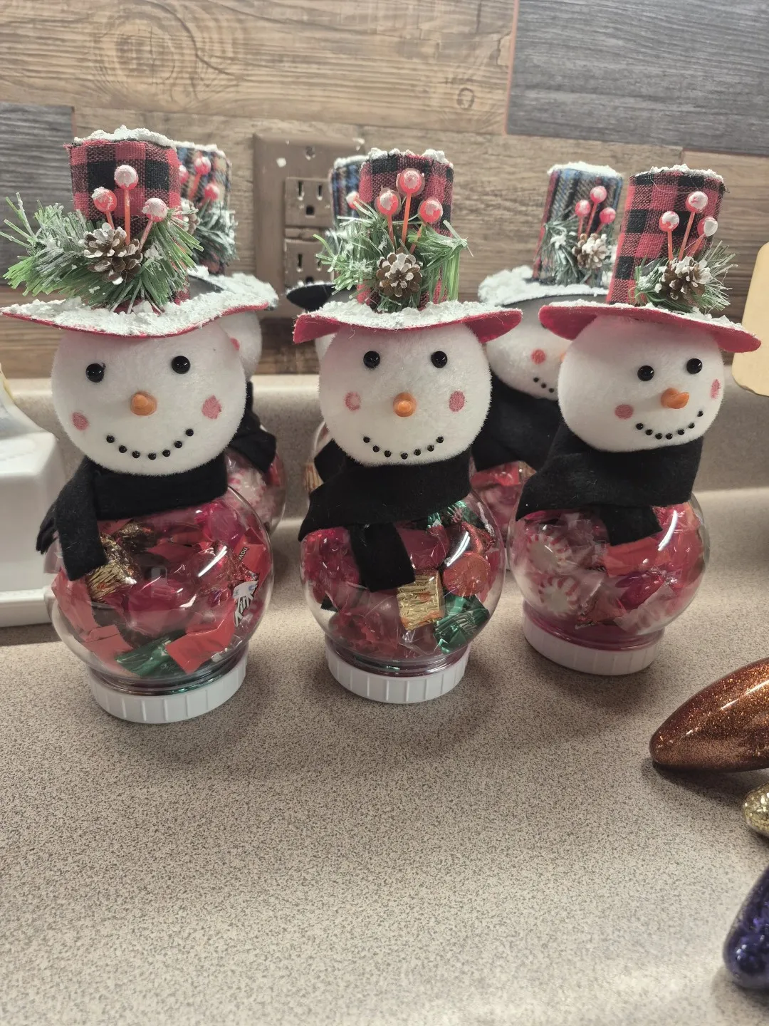Three containers, filled with candy, have tops that make them look like snowmen.