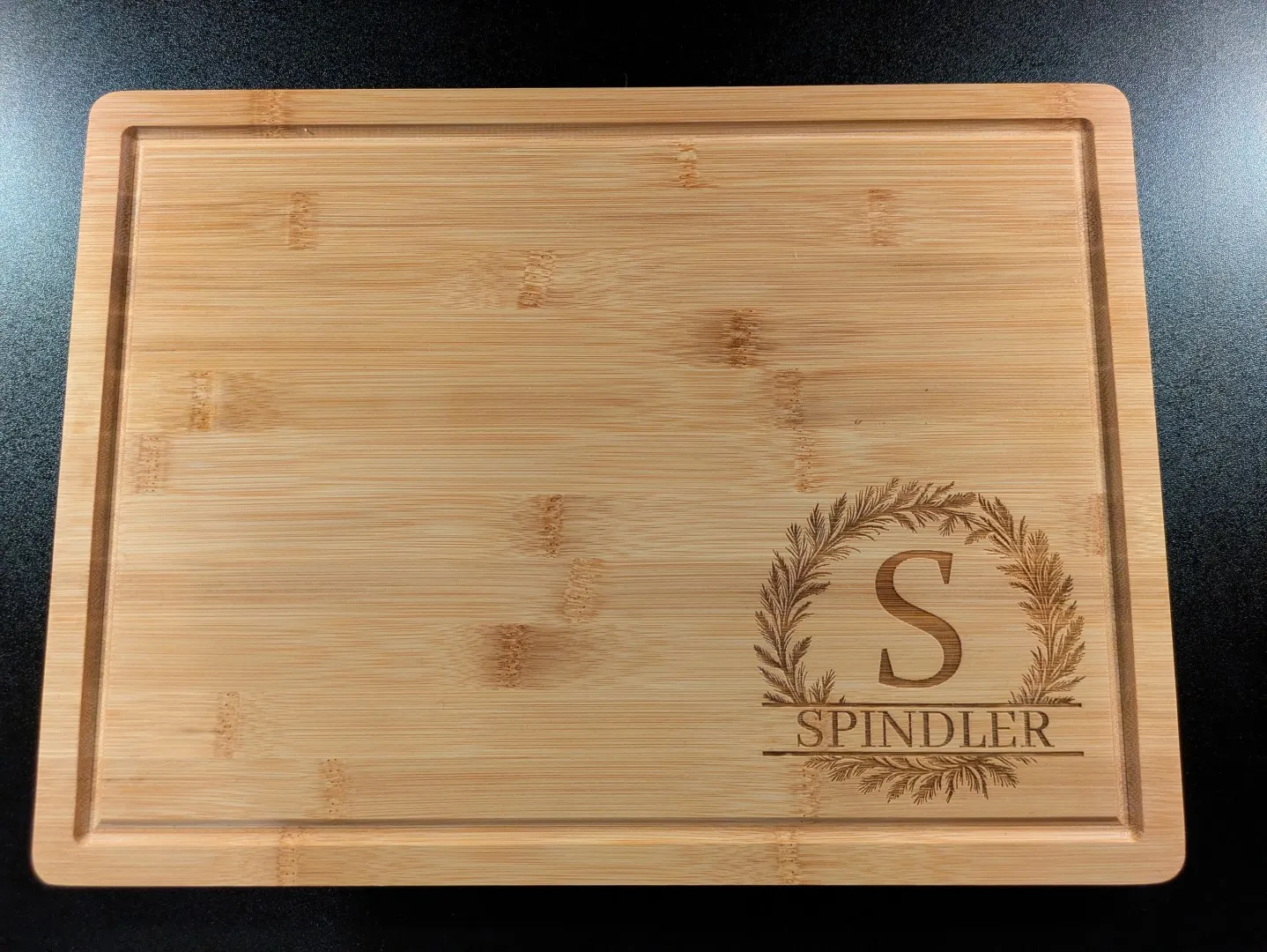 A wooden cutting board. In the corner, engraved into a wood, is an emblem with the letter S and the word 'Spindler'.