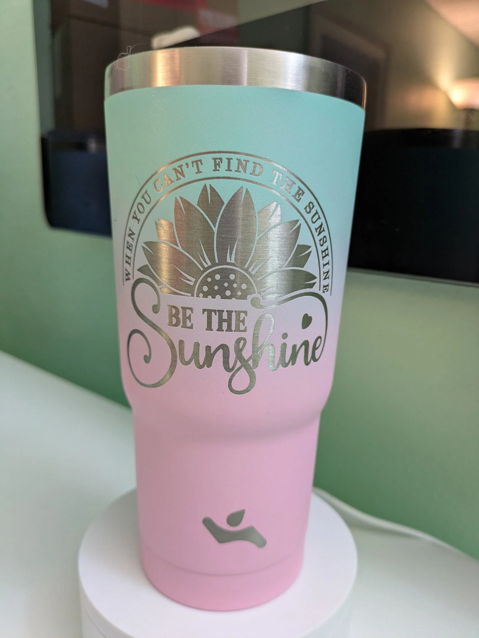 A tumbler with a gradient pattern, with blue on the top and pink on the bottom. Etched into the side of the tumbler is the phrase "When you can't find the sunshine, be the sunshine", with a picture of half of a sunflower.