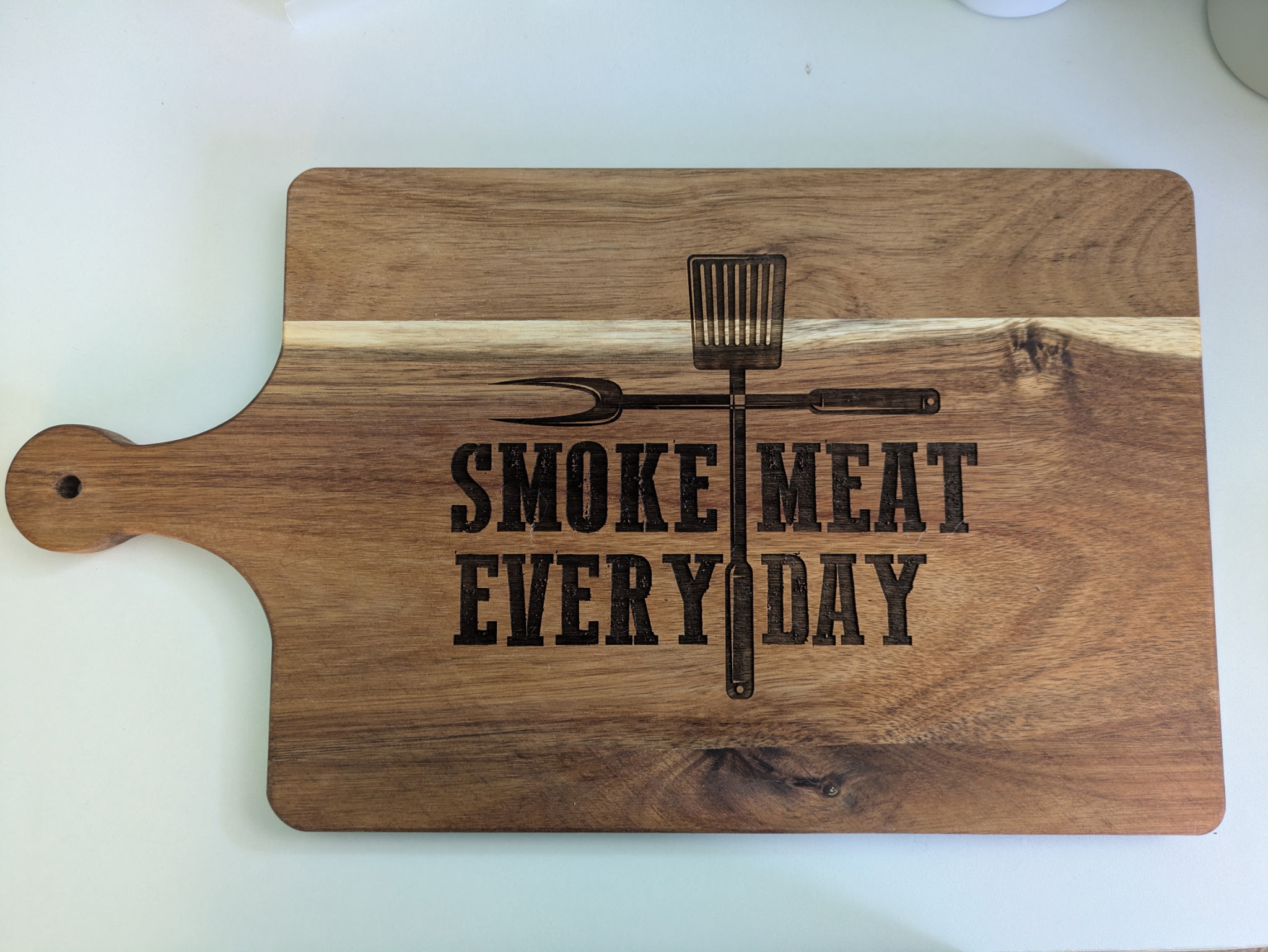 A wooden cutting board with the words "Smoke Meat Everyday" etched onto it.